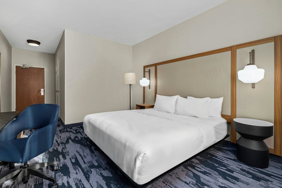 A hotel room with a large bed, a desk, a chair, a lamp, and a nightstand.