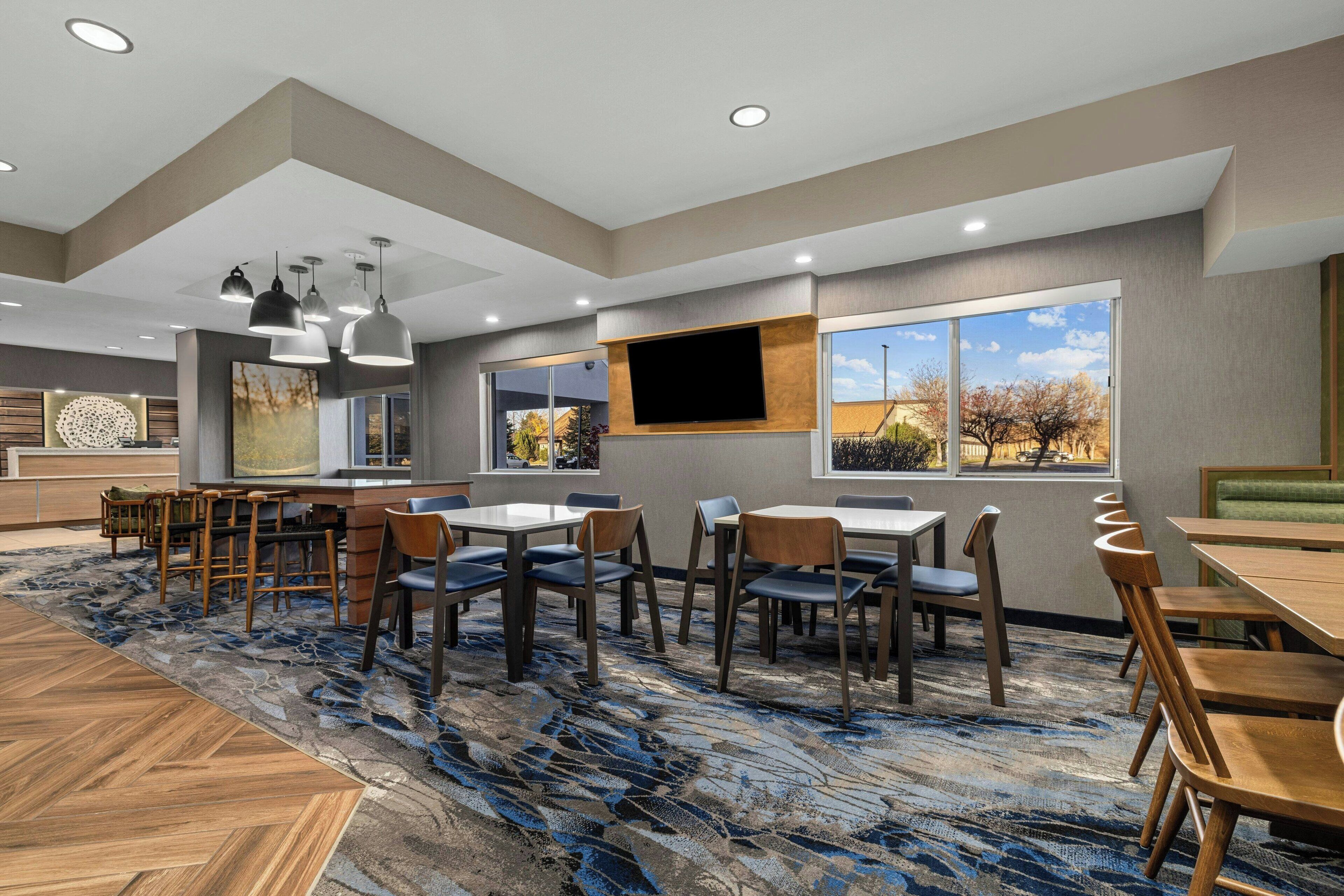 A hotel lobby with a large seating area, a flat-screen TV mounted on the wall, and a view of the outdoors through large windows.