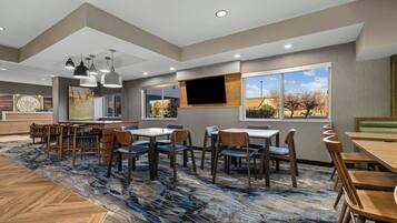 A hotel lobby with a large seating area, a flat-screen TV mounted on the wall, and a view of the outdoors through large windows.