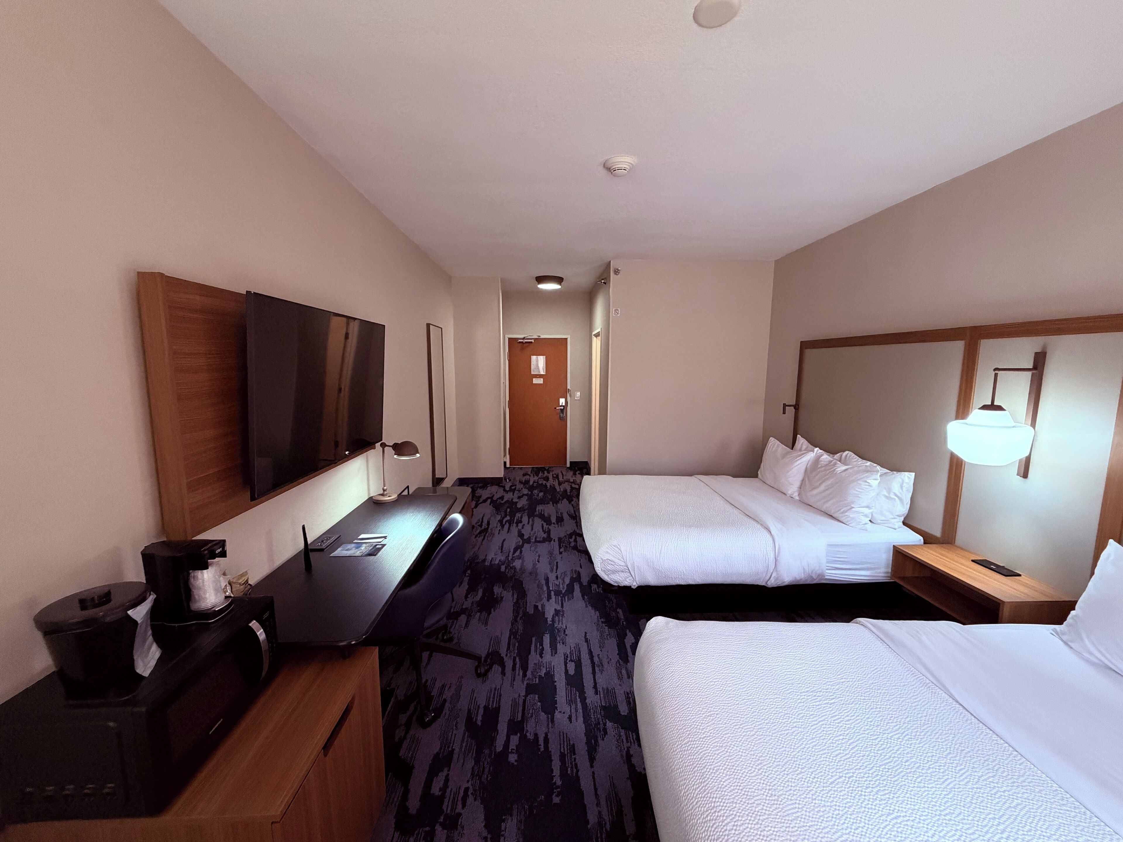 A hotel room with a bed, a desk with a computer, a TV, and a lamp.