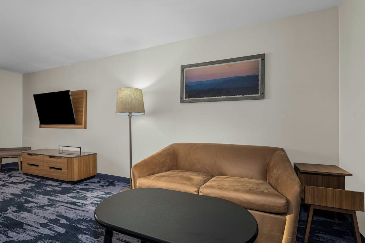 A modern hotel room with a leather sofa, a flat-screen TV, a lamp, and a painting on the wall.