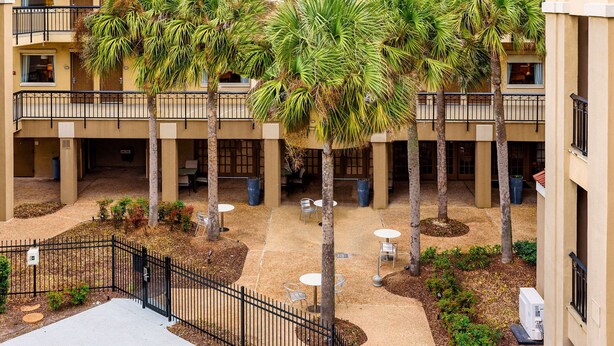 A multi-level courtyard with palm trees, outdoor seating, and a black metal fence. - Comfort Suites Baton Rouge South I-10 (Baton Rouge)