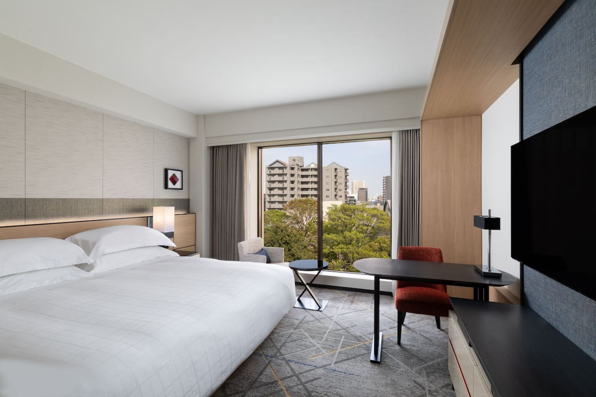 A hotel room with a large bed, a desk, a chair, and a TV.