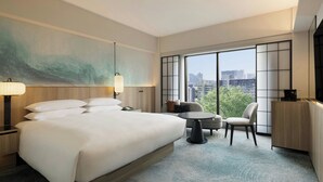 A hotel room with a large bed, a desk, a chair, a TV, and a view of the city through large windows. - Sheraton Miyako Hotel Tokyo (Tokyo)