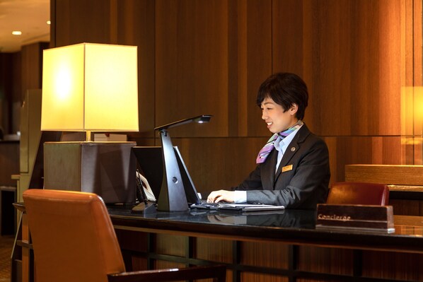 A hotel reception desk with a laptop, a lamp, and a nameplate.