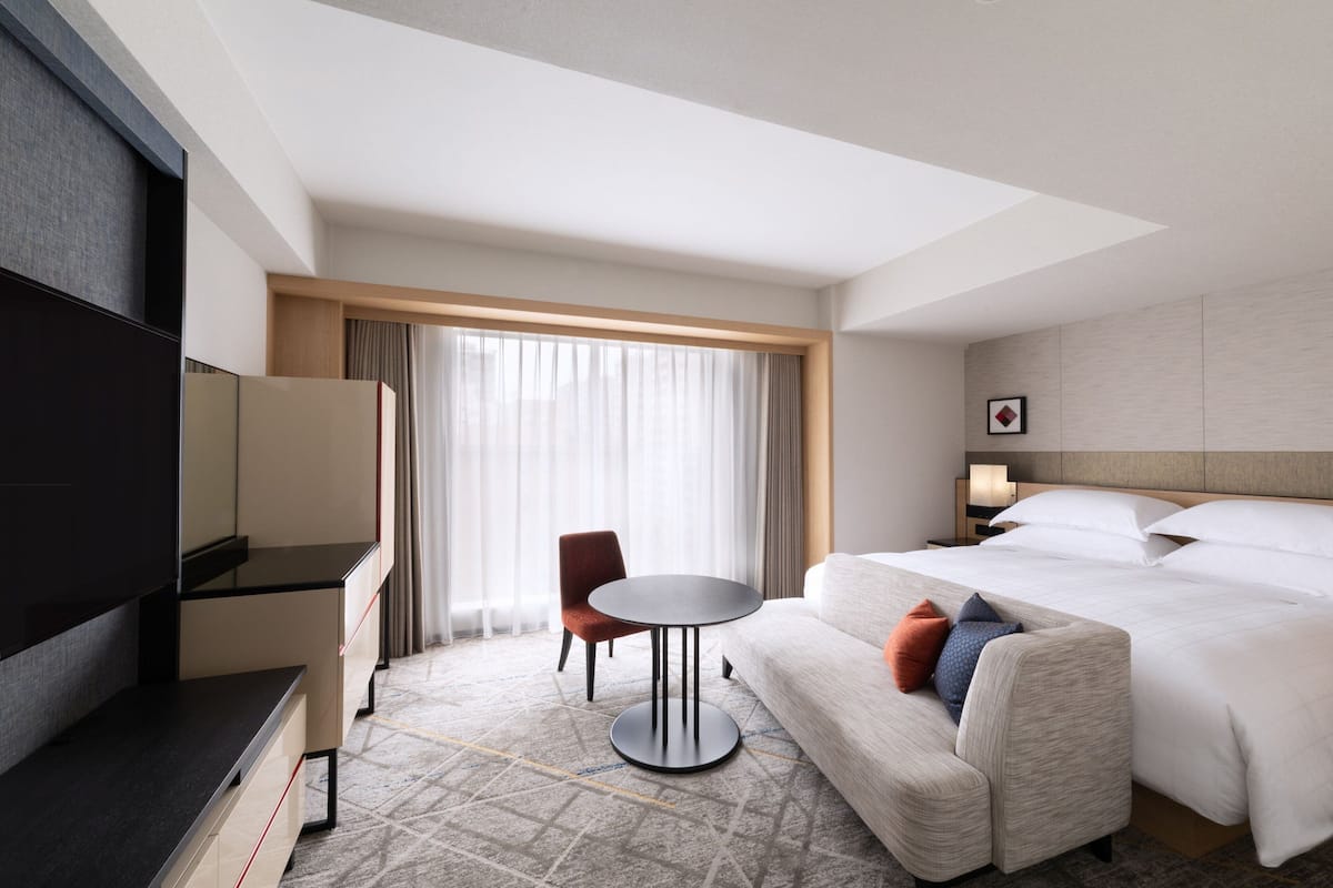 A hotel room with a bed, a sofa, a TV, a small table, and a chair.