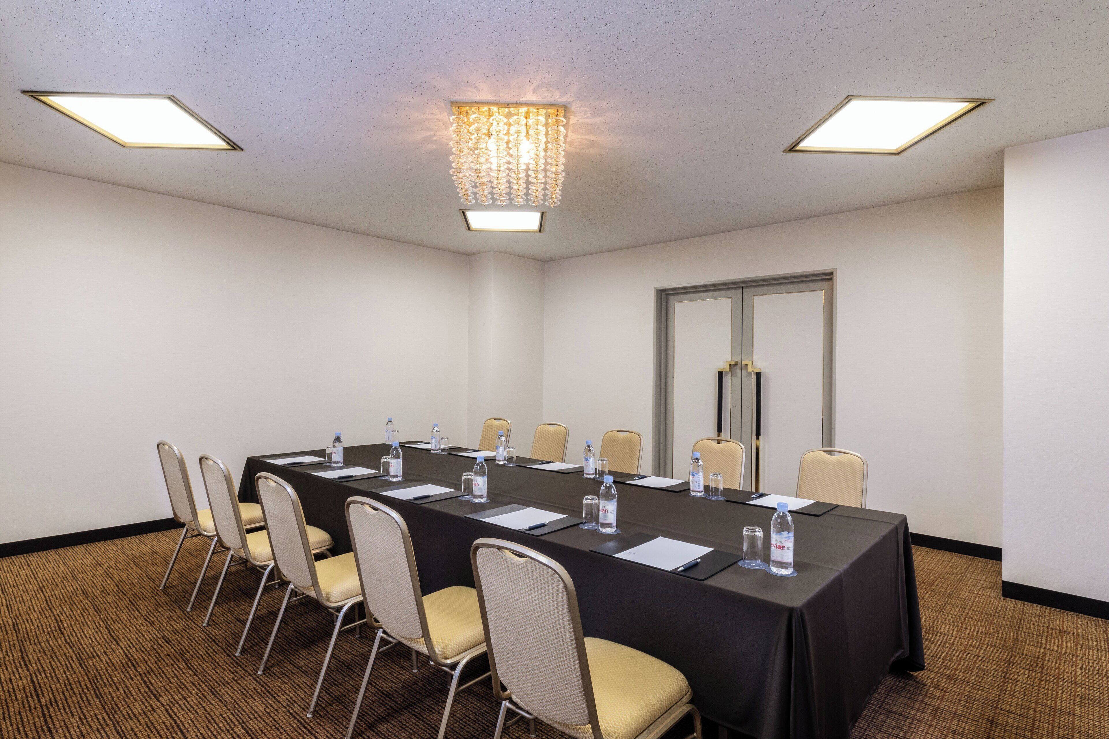 A conference room with a long table, chairs, water bottles, and a chandelier.