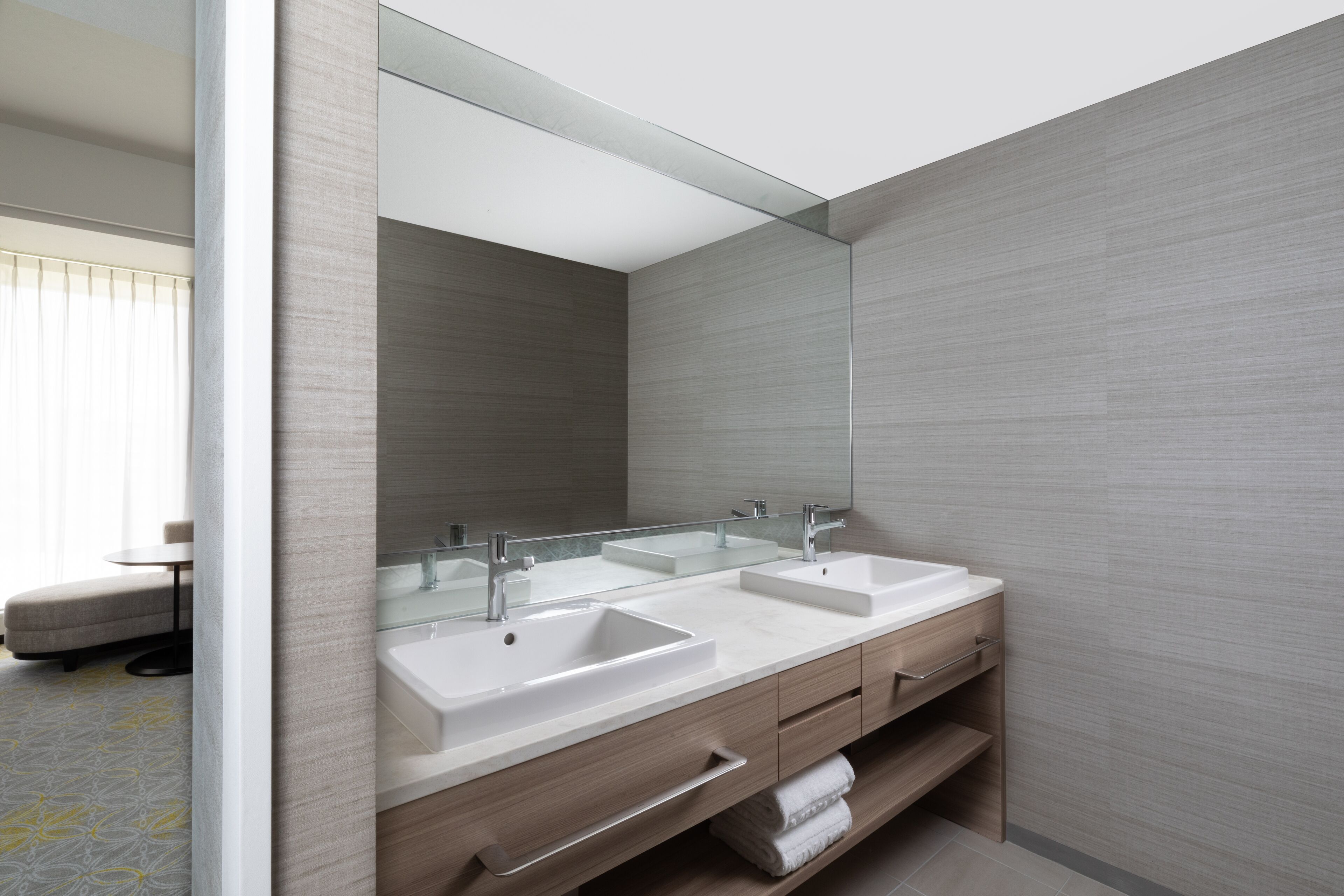 A modern bathroom with two sinks, a large mirror, and a glass partition.