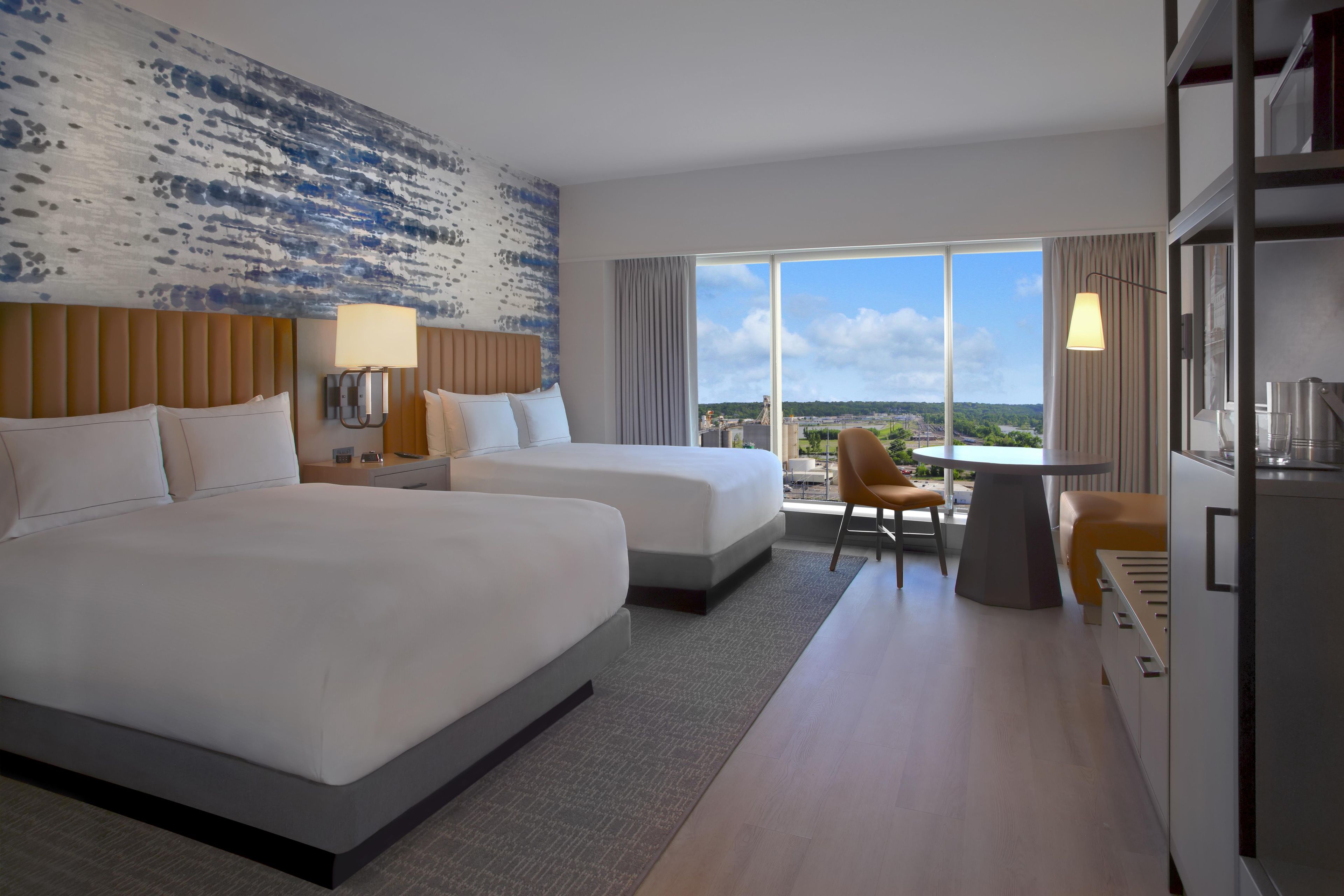 A hotel room with two beds, a desk, and a view of the city.