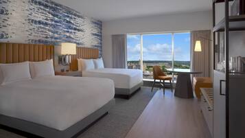 A hotel room with two beds, a desk, and a view of the city.