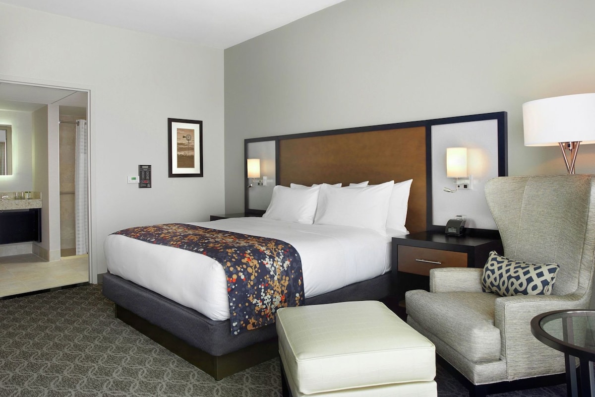 A hotel room with a bed, a chair, a small table, a mirror, and a picture on the wall.