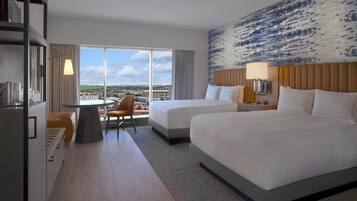 A hotel room with two beds, a dining table, a chair, and a view of the city.