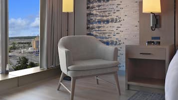 Una camera d'albergo con vista su un paesaggio lontano, una sedia moderna, un comodino con una lampada e una parete con motivo strutturato.