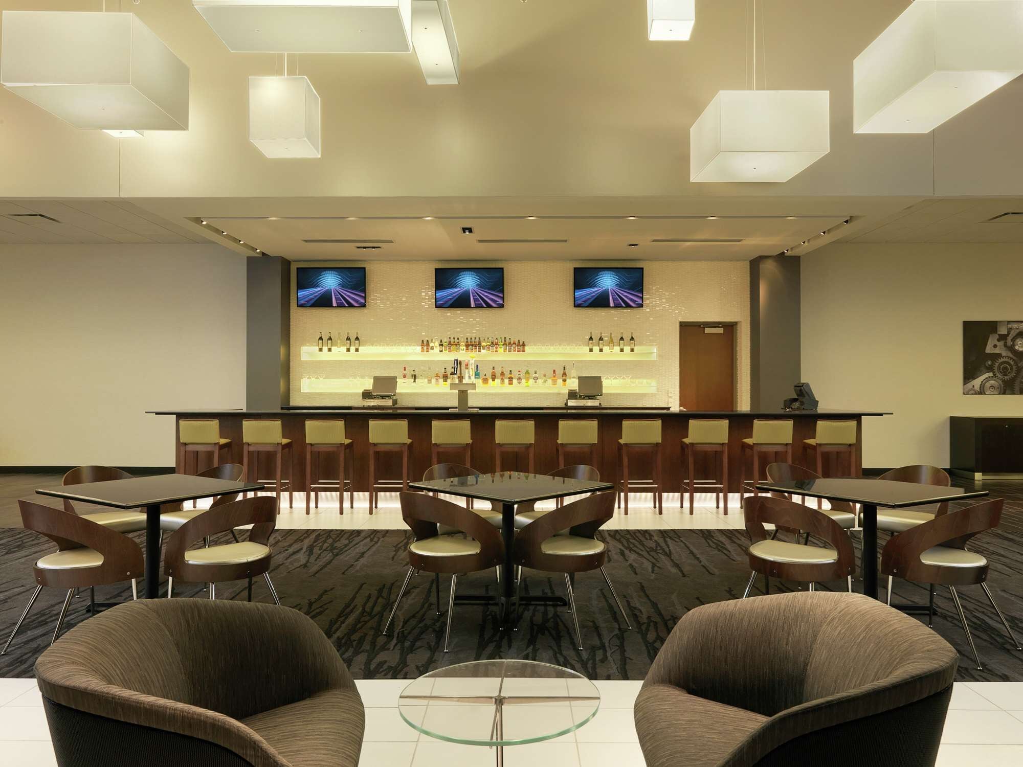 A modern bar area with a long counter, multiple seating options, and a television screen displaying a racing game.