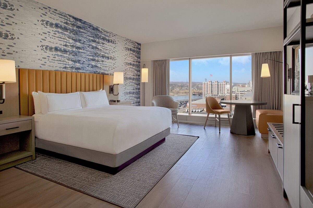 Habitación de hotel con una cama grande, un escritorio, una silla y vistas a la ciudad.