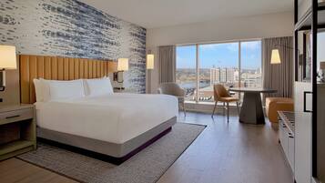 A hotel room with a large bed, a desk, a chair, and a view of the city.