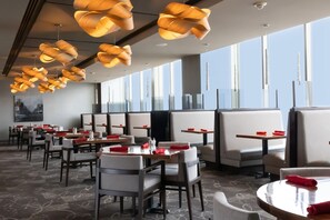 Un restaurante moderno con techos altos, lámparas colgantes de madera originales y grandes ventanales con vistas a la ciudad.