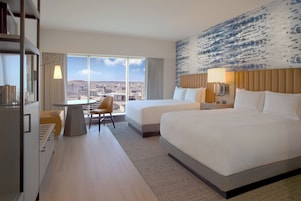 Habitación de hotel con dos camas, un escritorio y una silla. Amplia ventana con vista a la ciudad.