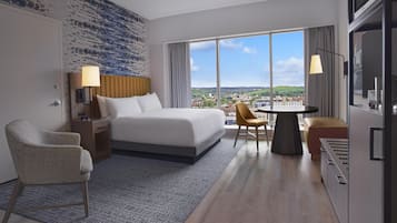 A hotel room with a large bed, a desk with a chair, a small table, and a view of a cityscape.