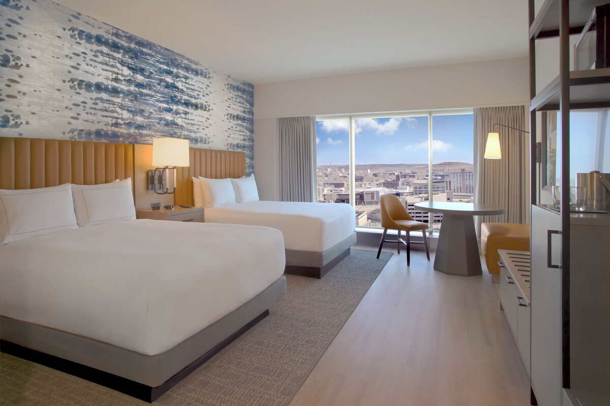 Habitación de hotel con dos camas, un escritorio y vista a la ciudad.