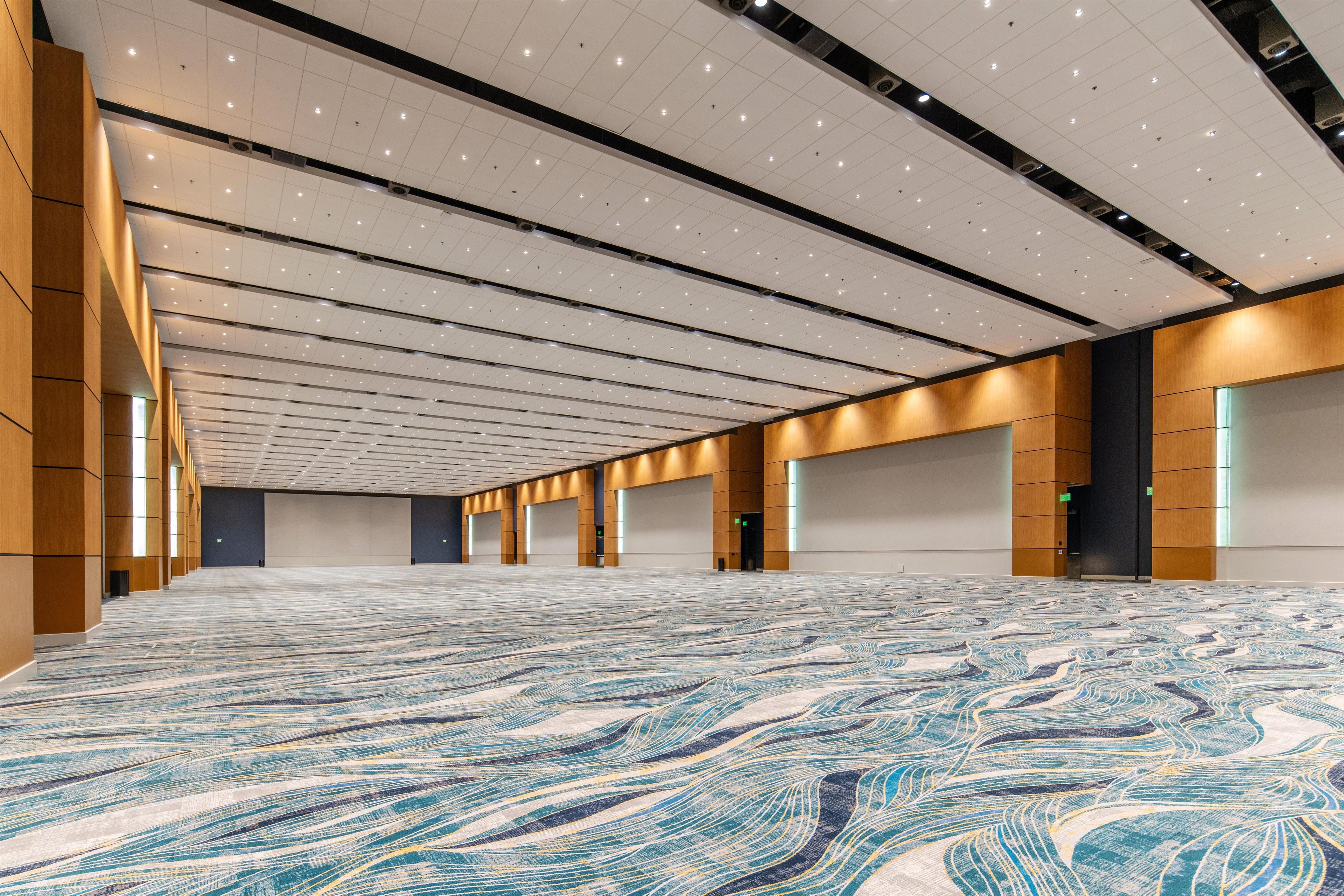 A spacious hall with a patterned carpet, multiple doors, and a high ceiling with recessed lighting.