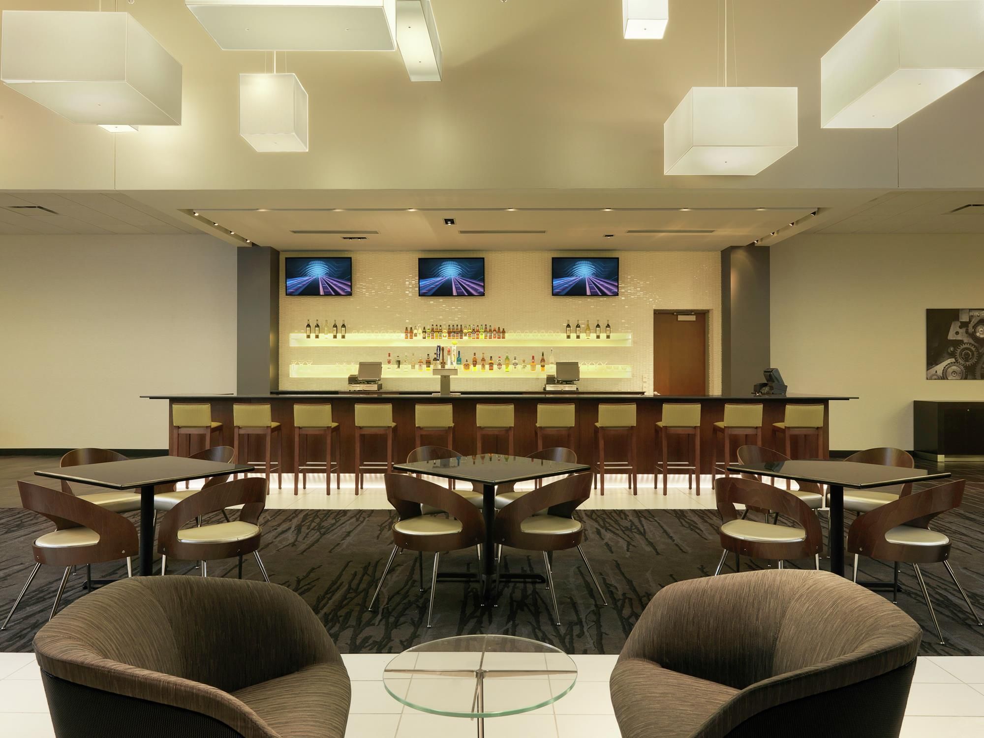A hotel lobby with a reception desk, bar area, seating arrangement, and a television screen displaying a sports channel.