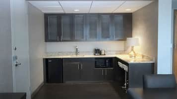A compact kitchen with dark cabinets, a microwave, a coffee maker, and a lamp on the countertop.