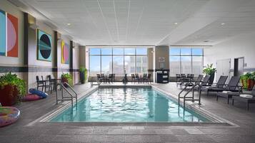 En indendørs swimmingpool med udsigt til byens skyline gennem store vinduer.