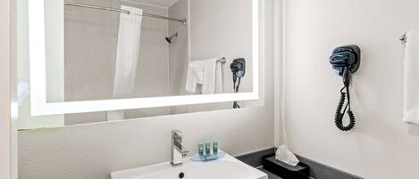 A bathroom with a large mirror, a sink, a towel rack, and a hairdryer mounted on the wall.