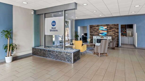 A reception area with a glass wall, a reception desk, a seating area with chairs, and a decorative wall with a clock. - Best Western Atlanta Cumberland/Galleria Hotel (Smyrna)
