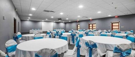 Un salón de conferencias con mesas redondas, cada una cubierta con manteles blancos y cintas azules, dispuestas en filas.