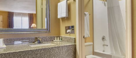 Un baño con lavamanos de granito, un espejo, un perchero para toallas, una ducha con cortina y un inodoro.