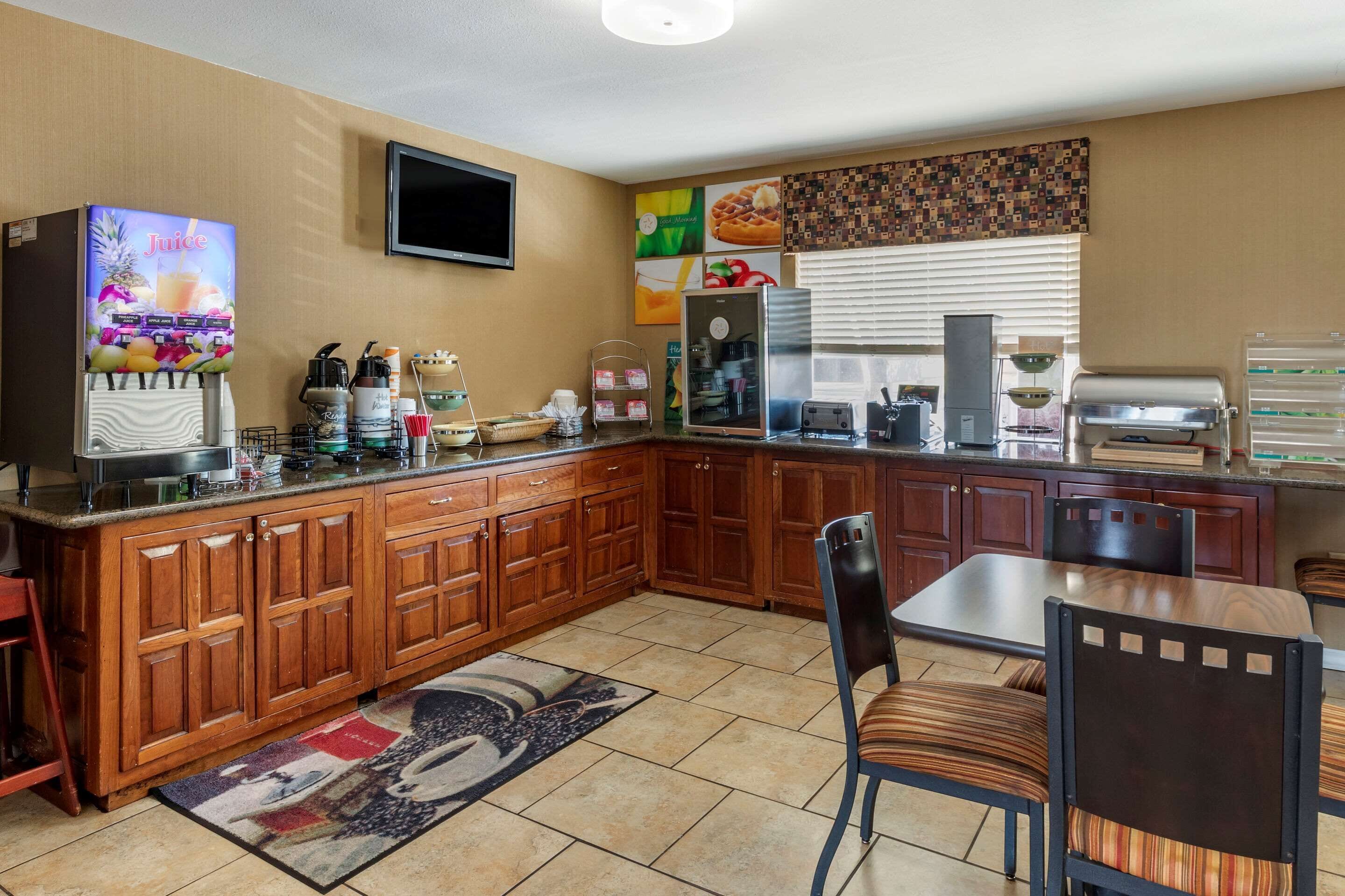 A kitchen with wooden cabinets, a coffee machine, a juice dispenser, and a television on the wall.