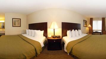 A hotel room with two beds, a nightstand with a lamp, a small table with a chair, and a window with curtains.