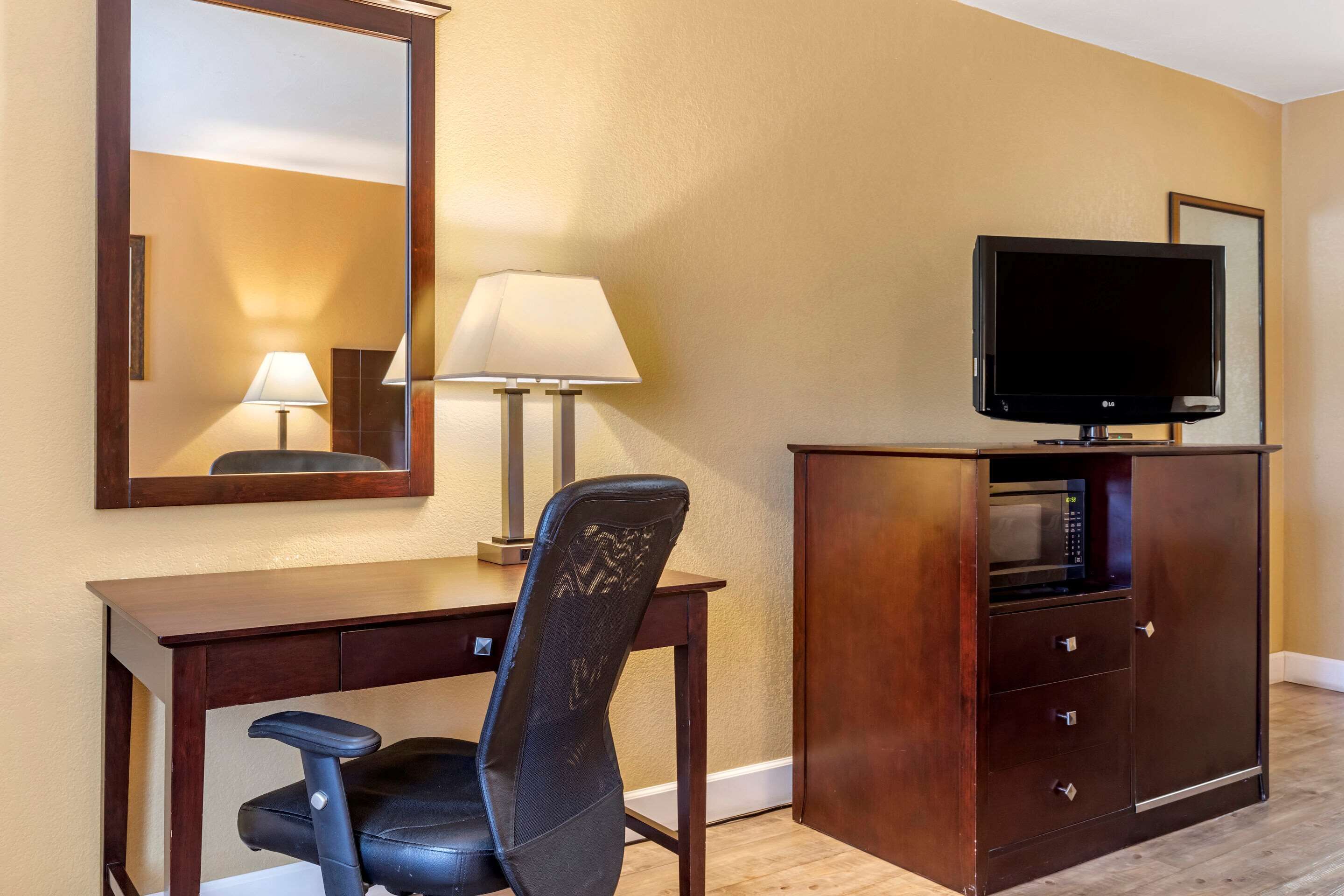 Habitación de hotel con un escritorio de madera, una silla de oficina negra, un televisor sobre un mueble y un espejo en la pared.