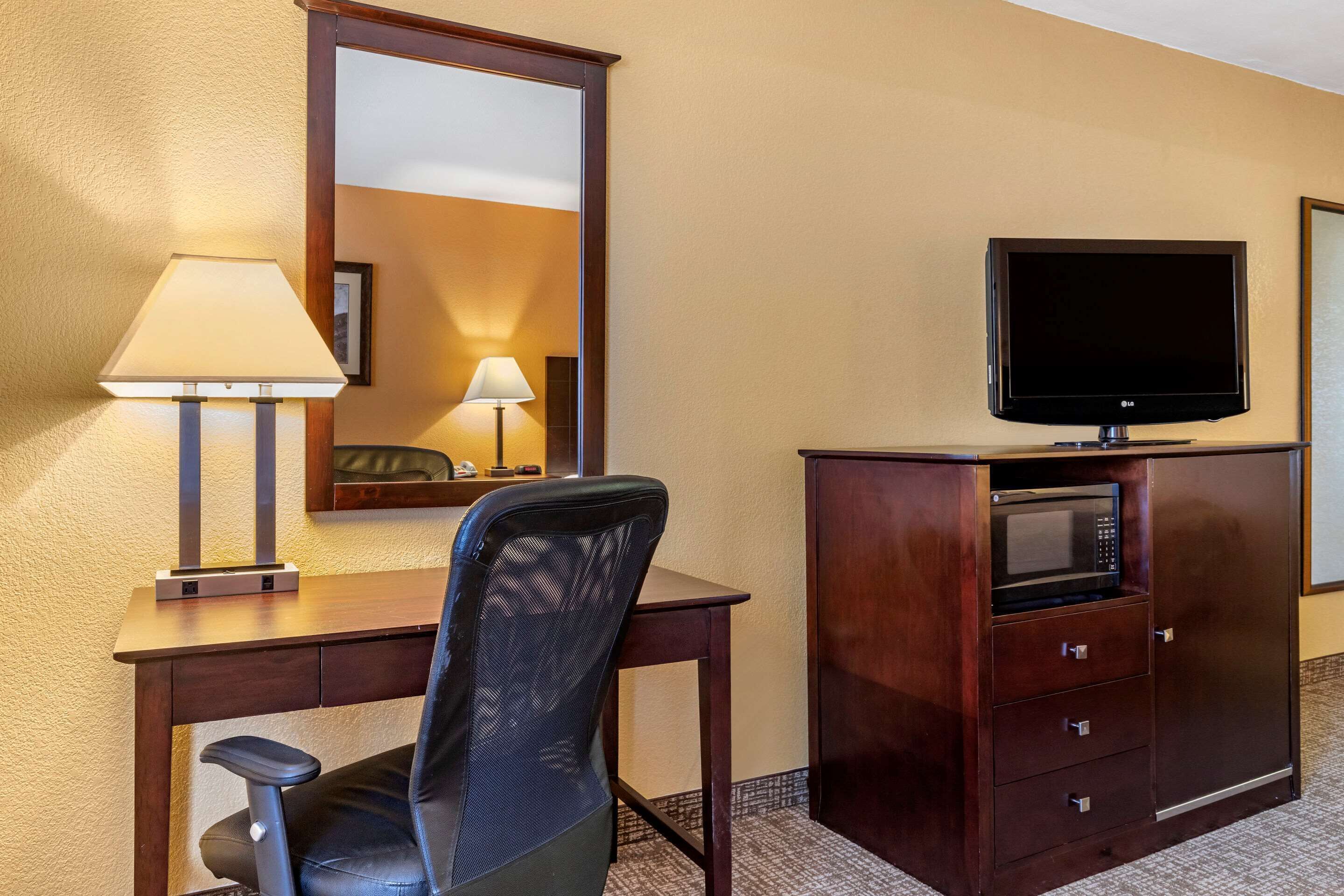 Habitación de hotel con escritorio, silla, televisión, microondas y espejo.