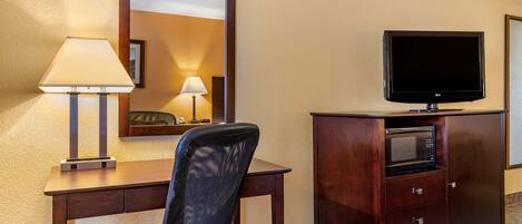 A hotel room with a desk, a chair, a television, a microwave, and a mirror.