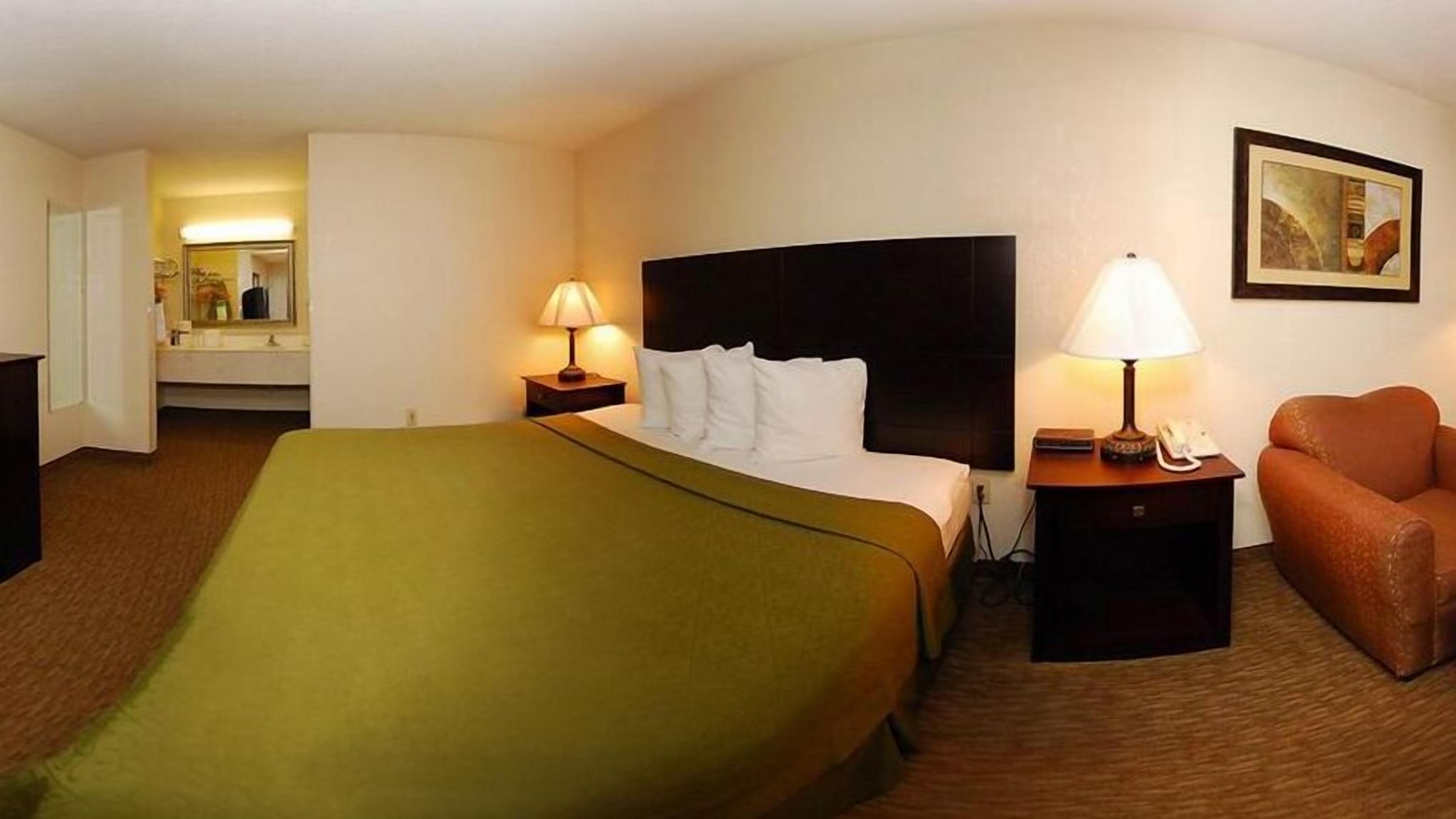 A hotel room with a bed, a desk, a chair, a lamp, a painting, and a bathroom.