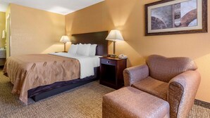 Une chambre d’hôtel avec un lit, deux lampes de chevet, une chaise et un tableau encadré au mur.