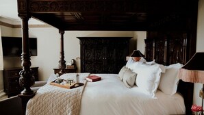 A four-poster bed with a tray of breakfast items, a bedside table with a lamp, and a dark wooden wardrobe.