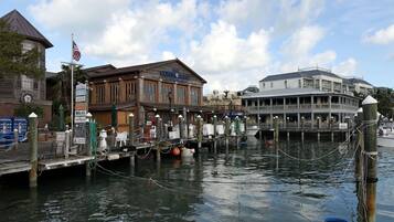 A waterfront restaurant with a dock extending into the water, a flagpole with an American flag, and a building with a sign reading "The Commodore Restaurant."