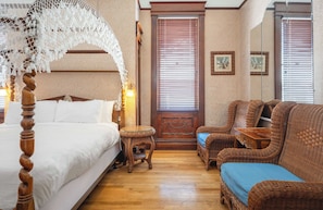 A bedroom with a four-poster bed, wicker furniture, and a wooden floor.