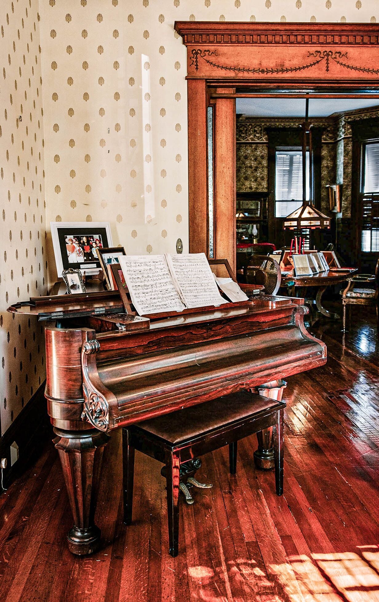 A grand piano in a room with patterned wallpaper and a large window.