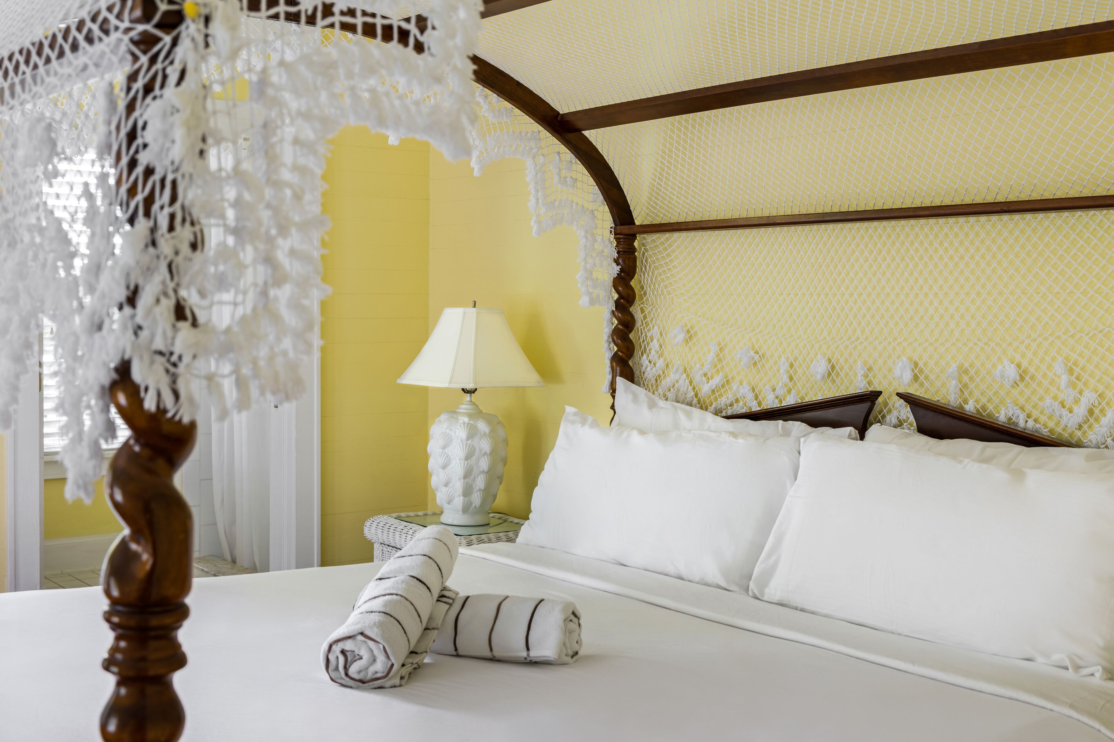 A neatly made bed with white linens, a white lamp on a bedside table, and a decorative canopy.