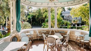 An outdoor patio with wicker furniture and a ceiling fan, surrounded by lush greenery and a view of a residential area. - Amsterdam's Curry Mansion Inn (Key West)