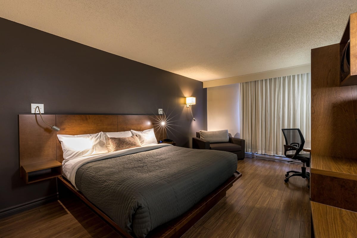 A hotel room with a large bed, bedside tables, a desk, a chair, and a window with curtains.