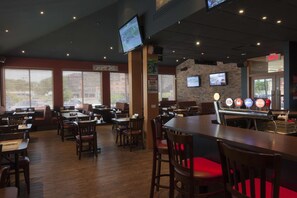 A restaurant with wooden tables and chairs, a bar area with a beer tap, and a television mounted on the wall.