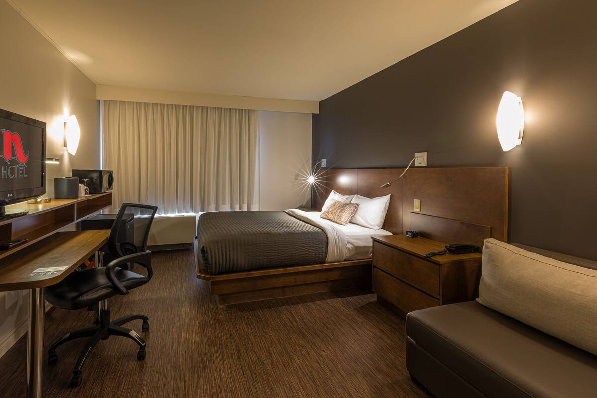 A hotel room with a bed, a desk, a chair, a sofa, and a TV.