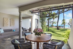 Un patio con mobiliario de mimbre, una mesa redonda con un jarrón de flores y vista al océano.
