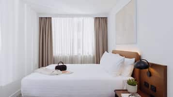 Una habitación de hotel con una cama bien hecha, una mesita de noche con una lámpara, una pequeña planta en maceta y un libro.